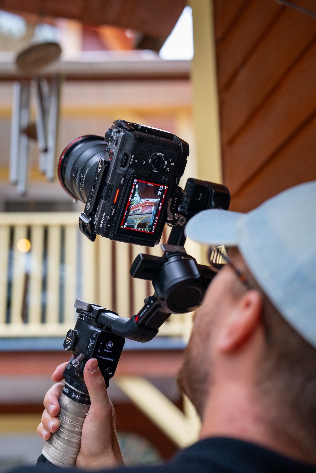 Tournage Astraeus: caméra Sony sur stabilisateur cadrant la façade d'une maison, vue par-dessus l'épaule du vidéaste