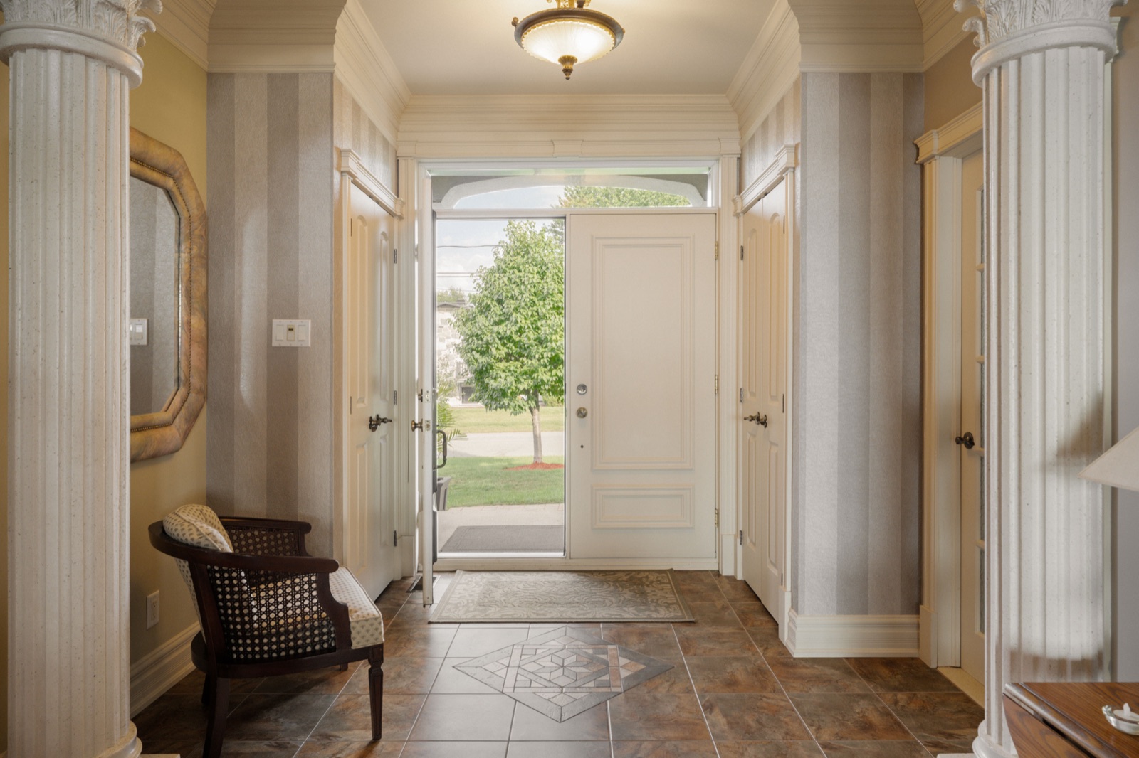 Foyer d'entrée à colonnes et papier peint rayé, porte blanche vitrée