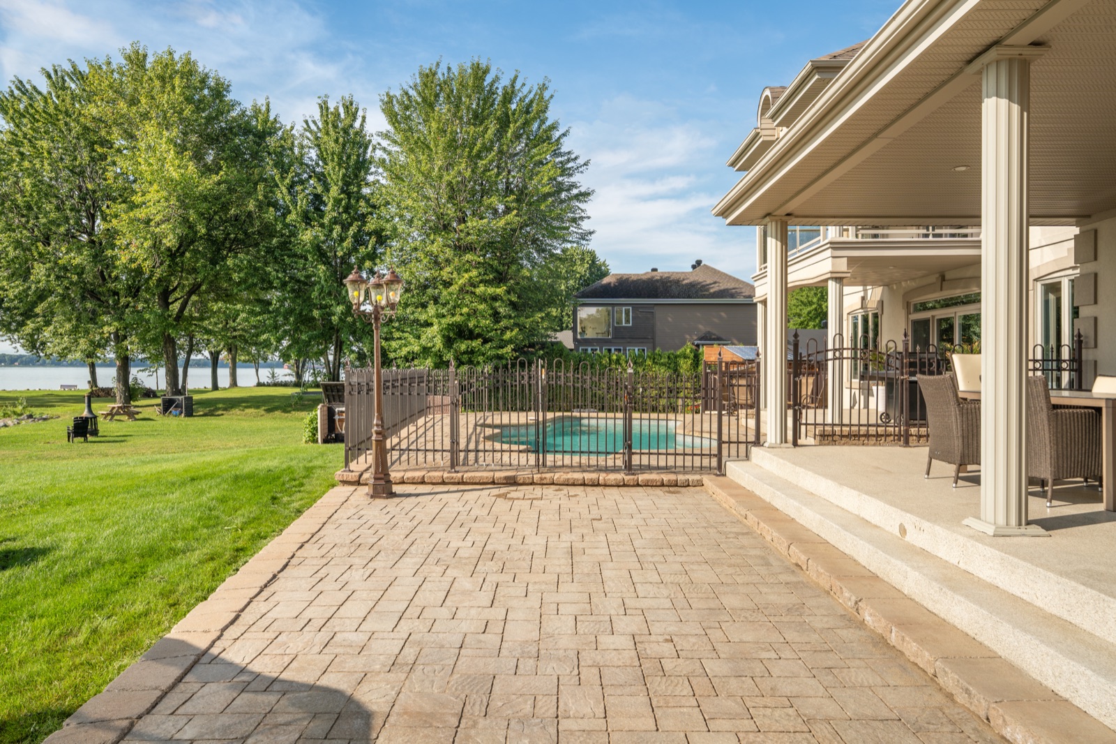 Terrasse de pavés sous le porche arrière, piscine clôturée et le fleuve au fond