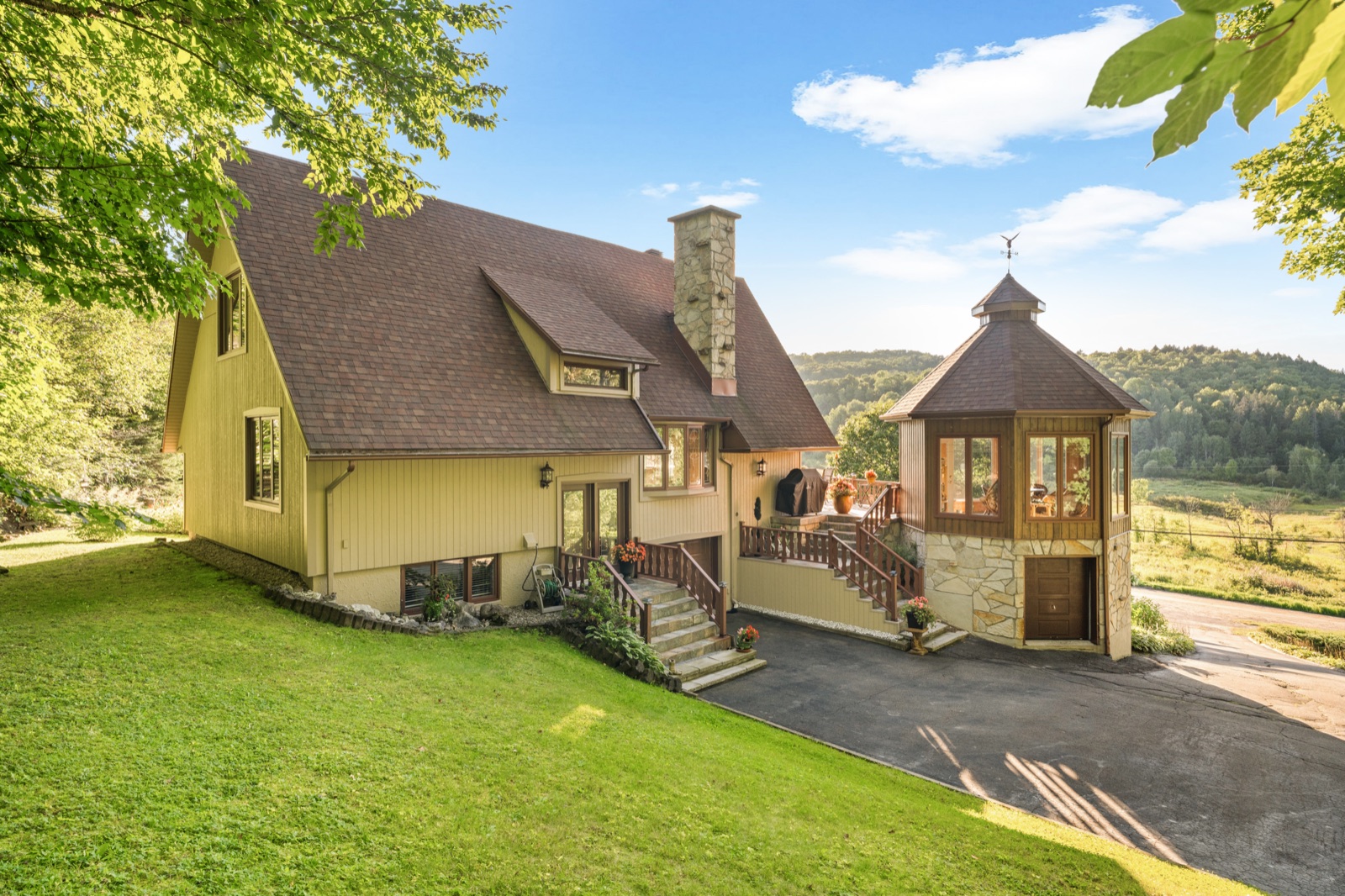 Façade du 9829 Chemin des Versants avec sa tourelle de pierre, la vallée en arrière-plan