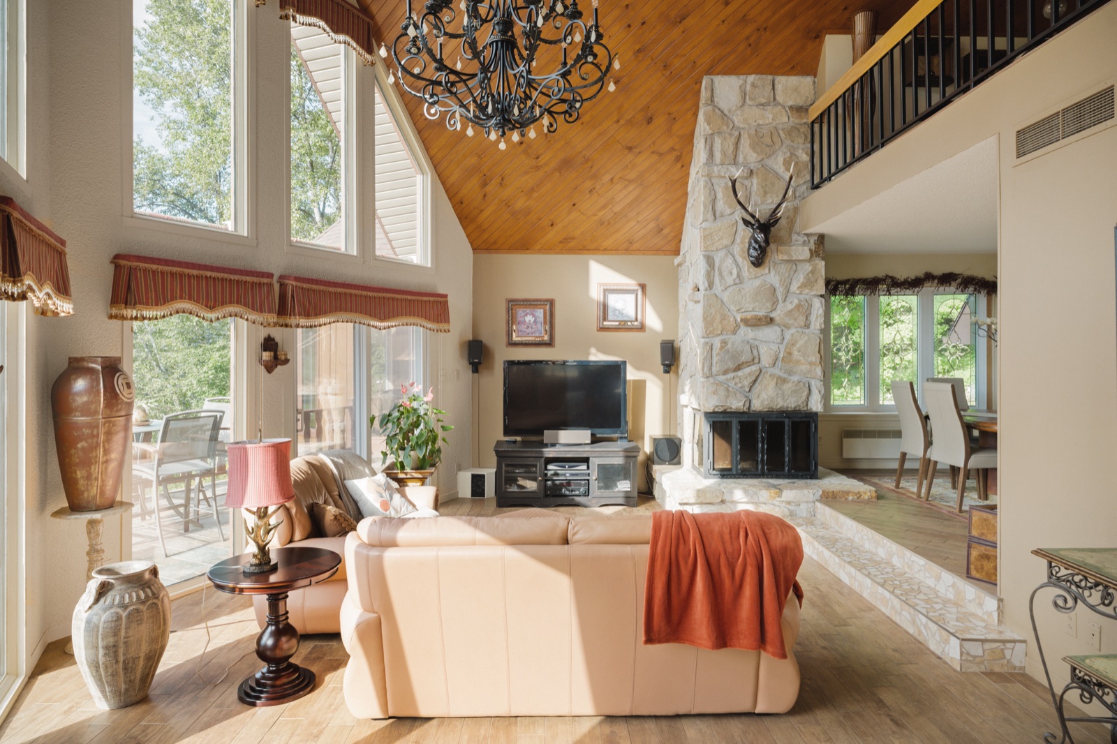Séjour au plafond de bois avec foyer de pierre sur deux étages et mezzanine à garde-corps de fer